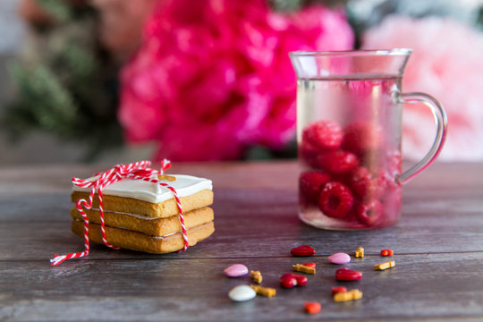 Baking Surprise Cookies with topping and icing on wooden background with pink heart and cap with malina drink