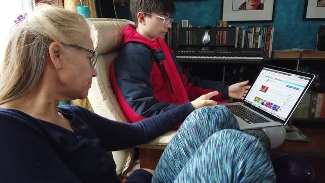 Closeup Of Mature Mother Pointing To A Computer Screen On Her Teen Son‚Äôs Lap And Talking.