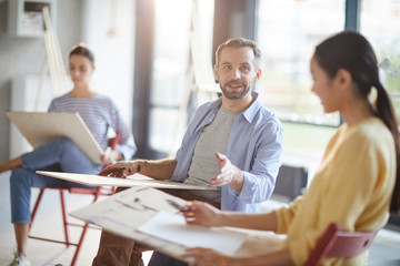 Young man with pencil and board explaining something or answering question of teacher at lesson of painting
