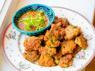 Deep fried fish pasty, Thai fish cake garnished with deep fried basil leaves serves with pickles which are cucumber slices