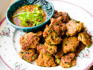 Deep fried fish pasty, Thai fish cake garnished with deep fried basil leaves serves with pickles which are cucumber slices