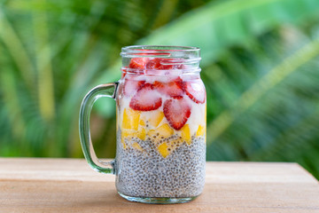 Almond milk chia pudding with fresh strawberries and mango in a glass jar mug. Vegan raw breakfast. Chia seeds and fresh cut fruits and berries dessert