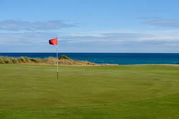 Golf flag on green with sea in background at Port Fairy golf course in Victoria Australia