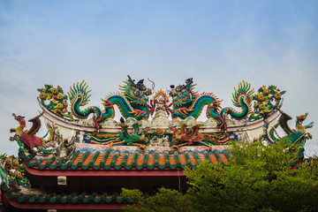 Beautiful two large grimace dragons crawling on decorative tiles roof in Chinese temple. Colorful roof detail of traditional Chinese temple with two dragon on blue sky background.