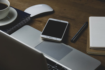 Top view table office with notebook, laptop, mobile, coffee cup, and pen with copy space on wooden table. Business concept.