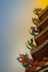 Beautiful large grimace dragons crawling on the decorative tile roof in Chinese temples. Colorful roof detail of traditional Chinese temple with dragon statue on blue sky background.