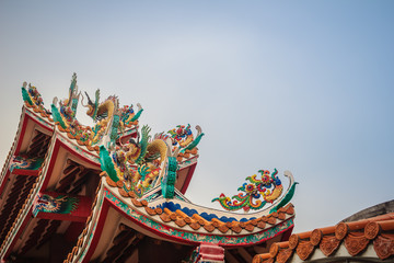Beautiful large grimace dragons crawling on the decorative tile roof in Chinese temples. Colorful roof detail of traditional Chinese temple with dragon statue on blue sky background.