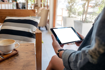 Mockup image of woman holding black tablet pc with blank screen with coffee cup on wooden table in cafe