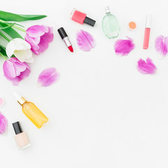 Obraz na płótnie Canvas Frame of tulips flowers and cosmetics, lipstick, nail polish on white background. Top view. Flat lay feminine desk.