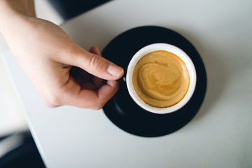 close up on hand holding cup of coffee on white table