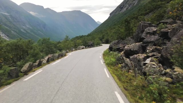 Point of view shot, driving on the Norwegian route 63, large rocks on both sides, towards The Trollstigen, on a cloudy, summer day, in Romsdal county, Rauma, Norway