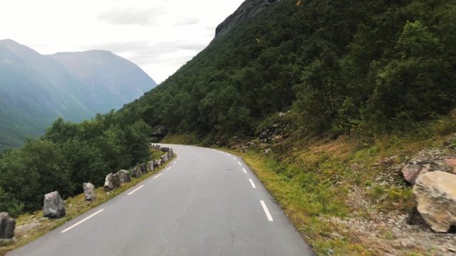 Point of view shot, driving on the Norwegian route 63, between steep mountains, towards The Trolls ladder, on a cloudy, summer day, in Romsdal county, Rauma, Norway