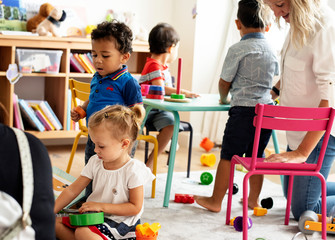 Nursery children playing with teacher in the classroom - obrazy, fototapety, plakaty