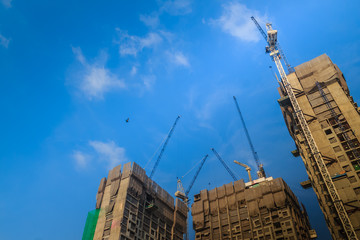 View of construction of multi-storey residential building. Condominium under construction with the luffing jib crane. High-rise skyscraper building construction site with crane against bright blue sky © kampwit
