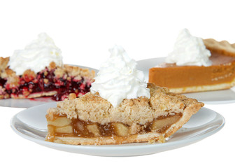 Close up on apple, cherry and pumpkin pie slices on individual plates with whipped cream on top of them, isolated on white. Focus on front pie, apple. National pie day march 14