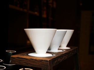 Three traditional ceramic coffee filters on wooden desk in a coffee shop. Slow Drip Coffee Maker, hand drip coffee