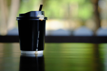 A black Paper coffee mug 16 oz. placed on a wooden table and coffee drip on mug.