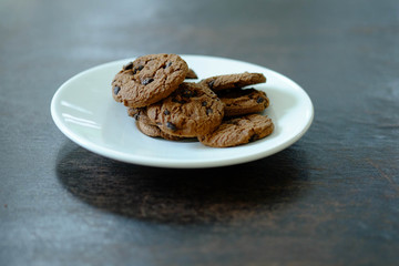 Close up Chocolate cookies in white dish on dark wooden table.
