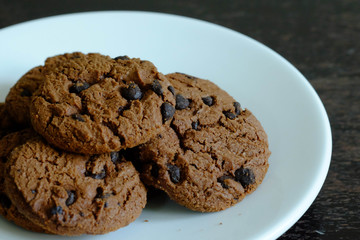Close up Chocolate cookies in white dish on dark wooden table.