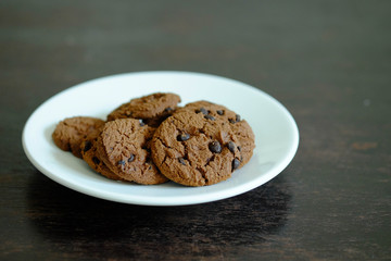 Close up Chocolate cookies in white dish on dark wooden table.