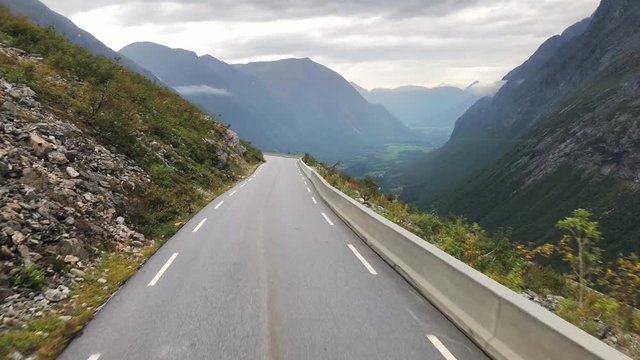 Slow motion shot, in a bus, down on curvy, narrow, Norwegian road 63, overlooking mountains and a valley, on a cloudy, overcast, spring day, in Rauma, Romsdal county, Norway