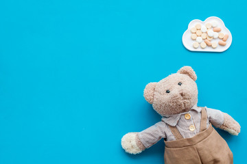 Childhood diseases concept. Treatment of children.Teddy bear toy and pills on blue background top view copy space