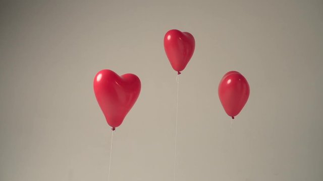 Three red heart shaped balloons floating in a studio