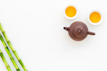Asian tea traditions. Drink tea. Tea pot near cups of green tea and bamboo decoration on white background top view space for text