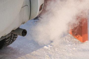 The car smokes in the winter. Smoke from a car pipe. The car is buzzing in the cold.