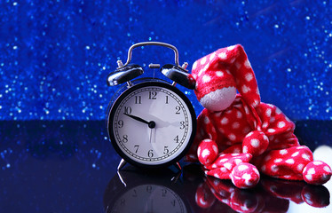 Alarm clock and doll on a blue background, bokeh effect. Twilight, night. The concept of relaxation, rest, sleep. Selective focus, close-up.