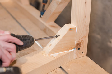 A man is screwing a screw into a wooden table. Carpentry workshop. Work with a screwdriver.