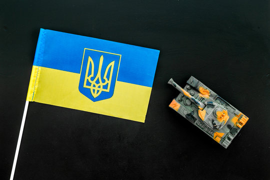 War, military threat, military power concept. Ukraine. Tanks toy near Ukrainian flag on black background top view