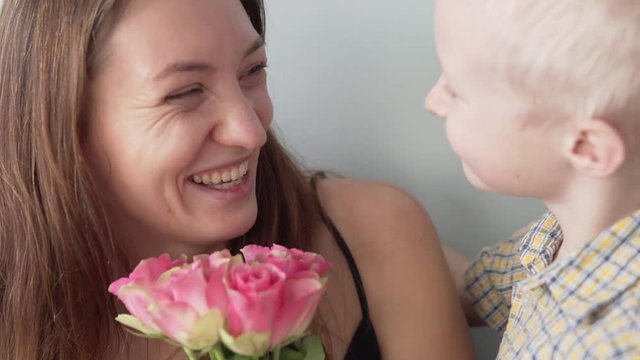 The boy gives a bouquet of small roses to his mother. The woman is very happy, she smiles and kisses the child. Close-up