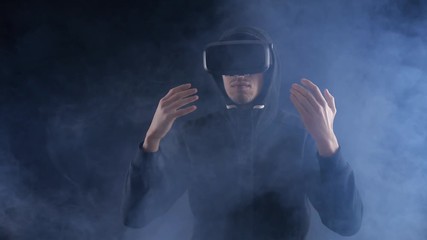 Man getting experience in using VR-headset on dark smoky background. Augmented reality device creating virtual space.