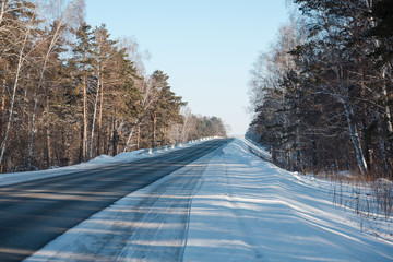 Asphalt road in winter in the forest. Asphalt under the snow. Road in the snow. Winter road.