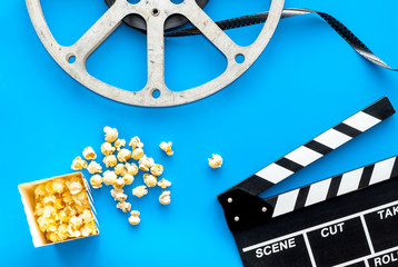 Cinema concept. Clapperboard, film stock, popcorn on blue background top view