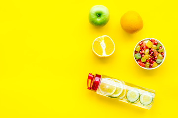 Diet rich in fruits. Slimming diet. Fruit salad near fruit lemon and cucumber water on yellow background top view copy space