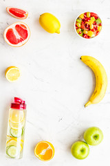 Diet rich in fruits. Slimming diet. Fruit salad near fruit lemon and cucumber water on white stone background top view copy space