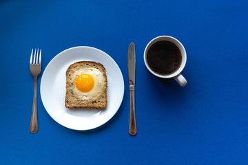 Breakfast concept. White plate with baked bread and egg and white coffee cup. Blue background.