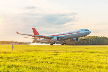 Evening airport and landing aircraft gear touching the runway with white smoke