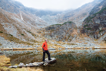 The young man of sporting physique stands on a mountain near the lake