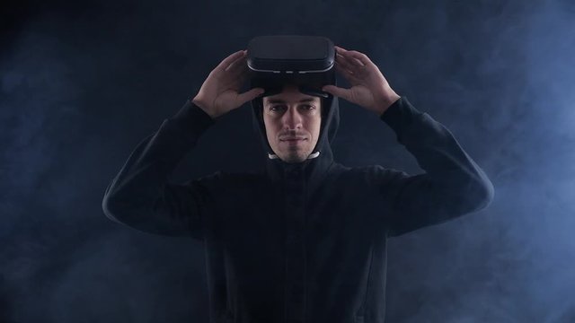 Futuristic man in hood Wearing VR Headset. Futuristic man using Virtual Reality Glasses in a dark smoky room.