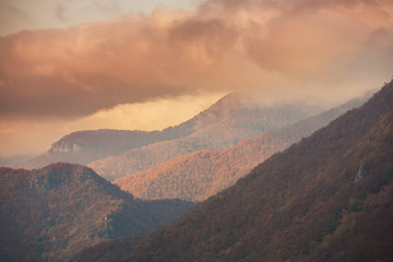 Beautiful autumn scenery in the mountains with mist clouds, pine trees and colorful foliage
