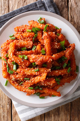 Asian honey chilli potato wedges with hot sweet sauce, sesame and green onions close-up. Vertical top view