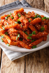 Delicious honey chilli potatoes with sesame and green onions served on a plate. vertical