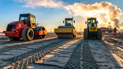 roller compacts soil in embankment on the highway construction. sand consolidation on road. Compactor driving on sandy. wheel marks on the sand - Powered by Adobe