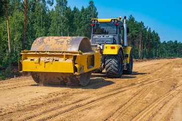 Pneumatic-tired roller compacts the soil in the embankment on the road's construction. sand...