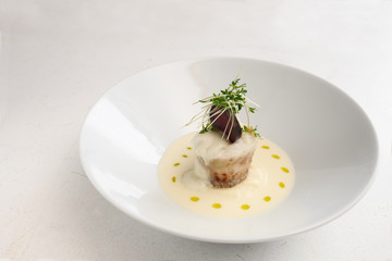 pike roll with beetroot and cress garnish in a creamy sauce in a deep bowl on a rustic white table, copy space
