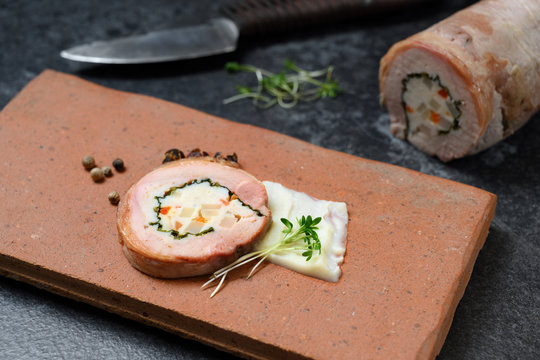 quail galantine, de-boned stuffed meat for a festive dinner served on a rustic brick plate on a dark table, copy space