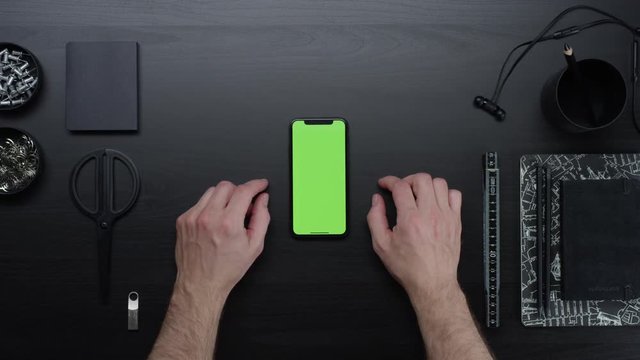 Male hands using smart device with green screen chroma on black clean minimalistic table with top view